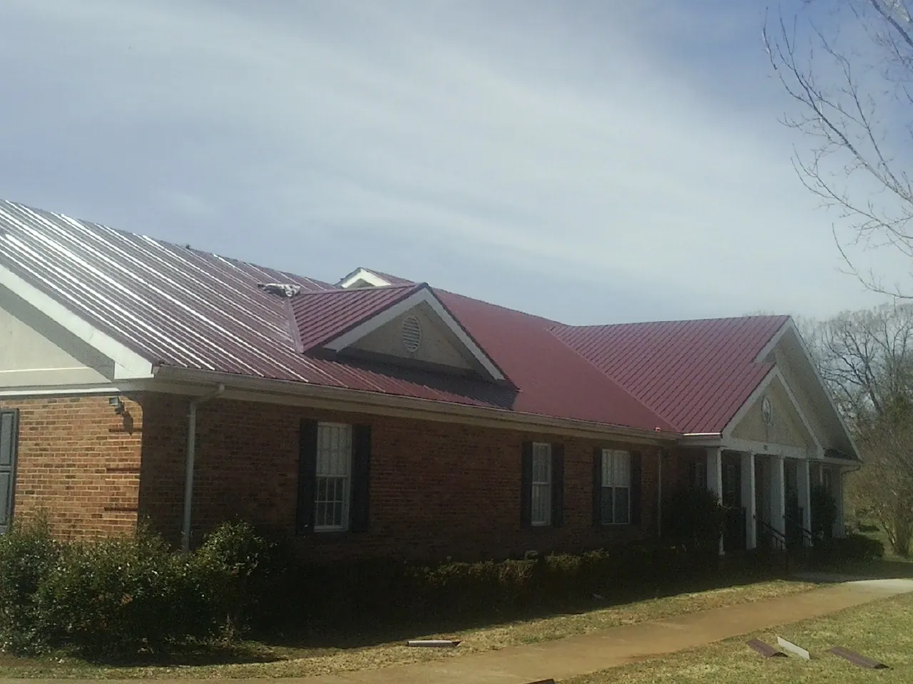 Red metal roof with gabled entries on a long brick building, from a Hail Damage Roof Repair job in Callensburg