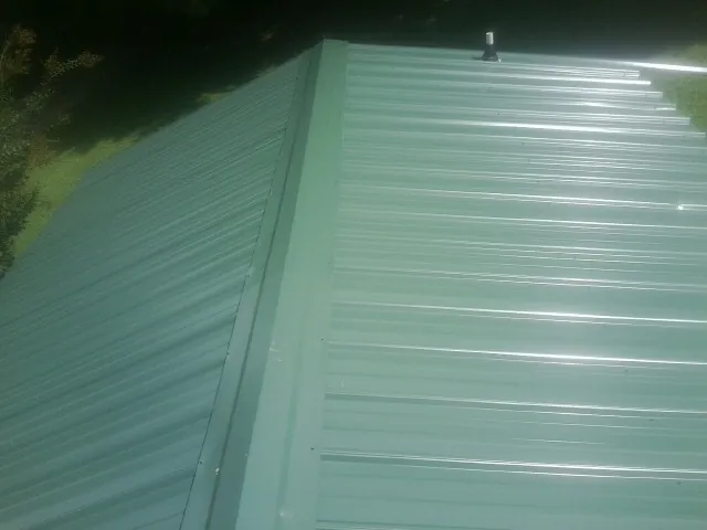 New green metal panels meeting at the ridge of a roof — Flat Roof Repair work by our crew in Callensburg