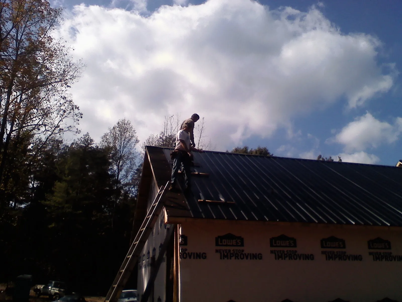 Roofer fastening dark metal panels high against a cloudy sky, from a Roof Inspection job in Callensburg