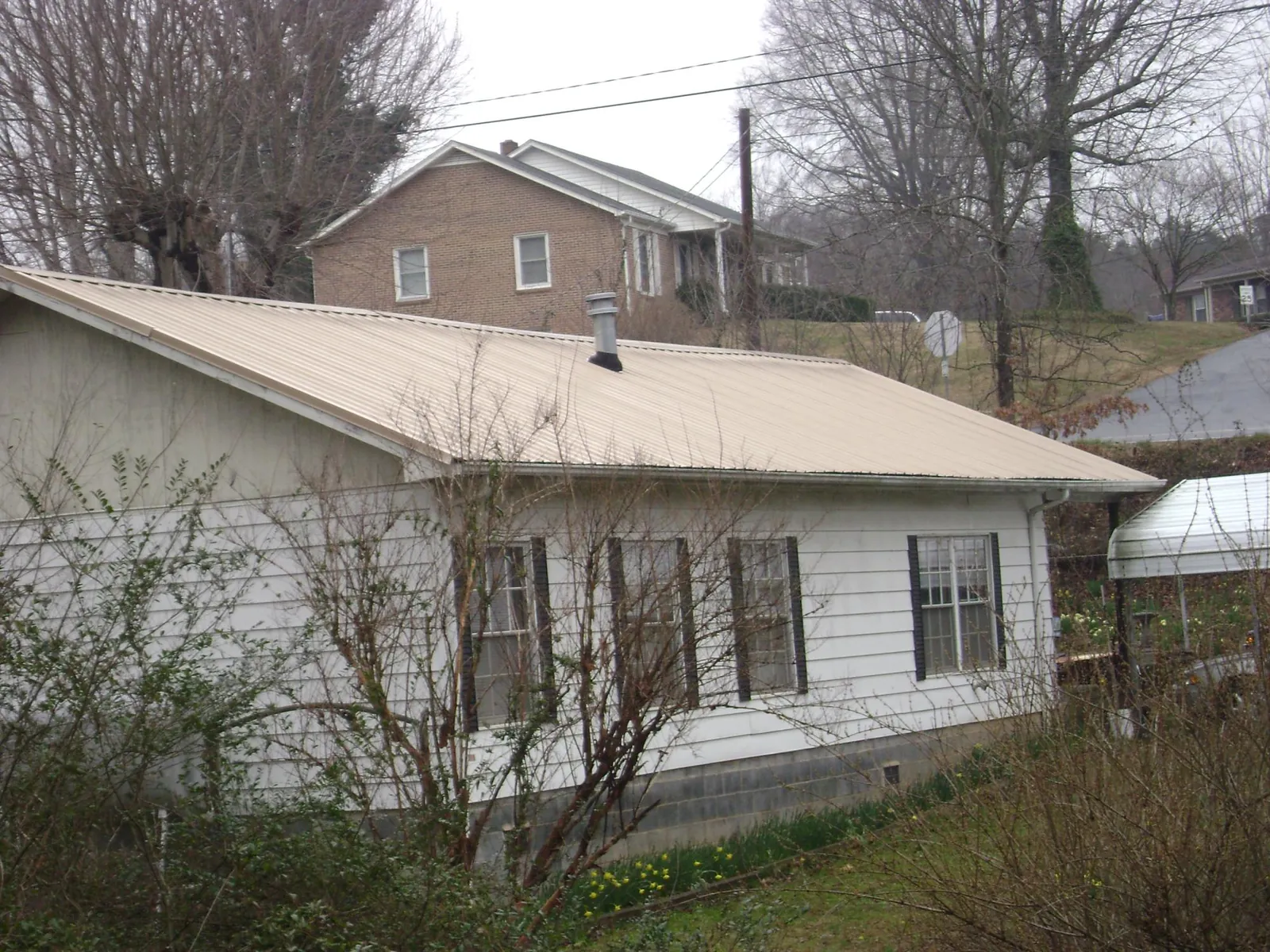 Tan metal roof on a white sided house set into a hillside — Commercial Roofing by Roofing Brothers in Callensburg