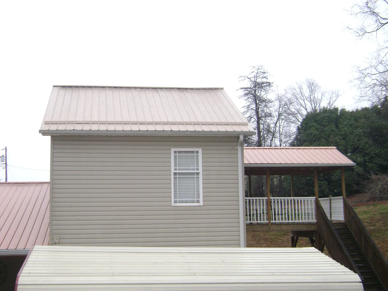 Tan metal roofs on a two story addition and attached porch, from a Roof Replacement job in Callensburg
